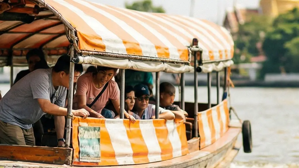 Bateau express aux couleurs vives accostant à un embarcadère en bois sur le fleuve Chao Phraya à Bangkok, avec un temple bouddhiste flou en arrière-plan
