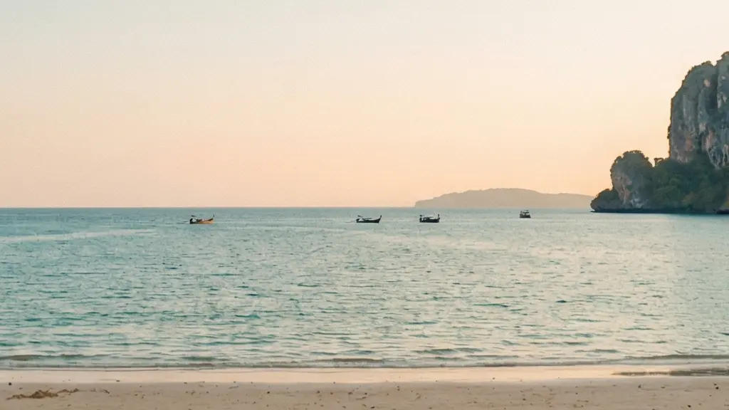Plage tropicale bordée de falaises au soleil de fin d’après-midi, avec très peu de visiteurs et de bateaux au loin.
